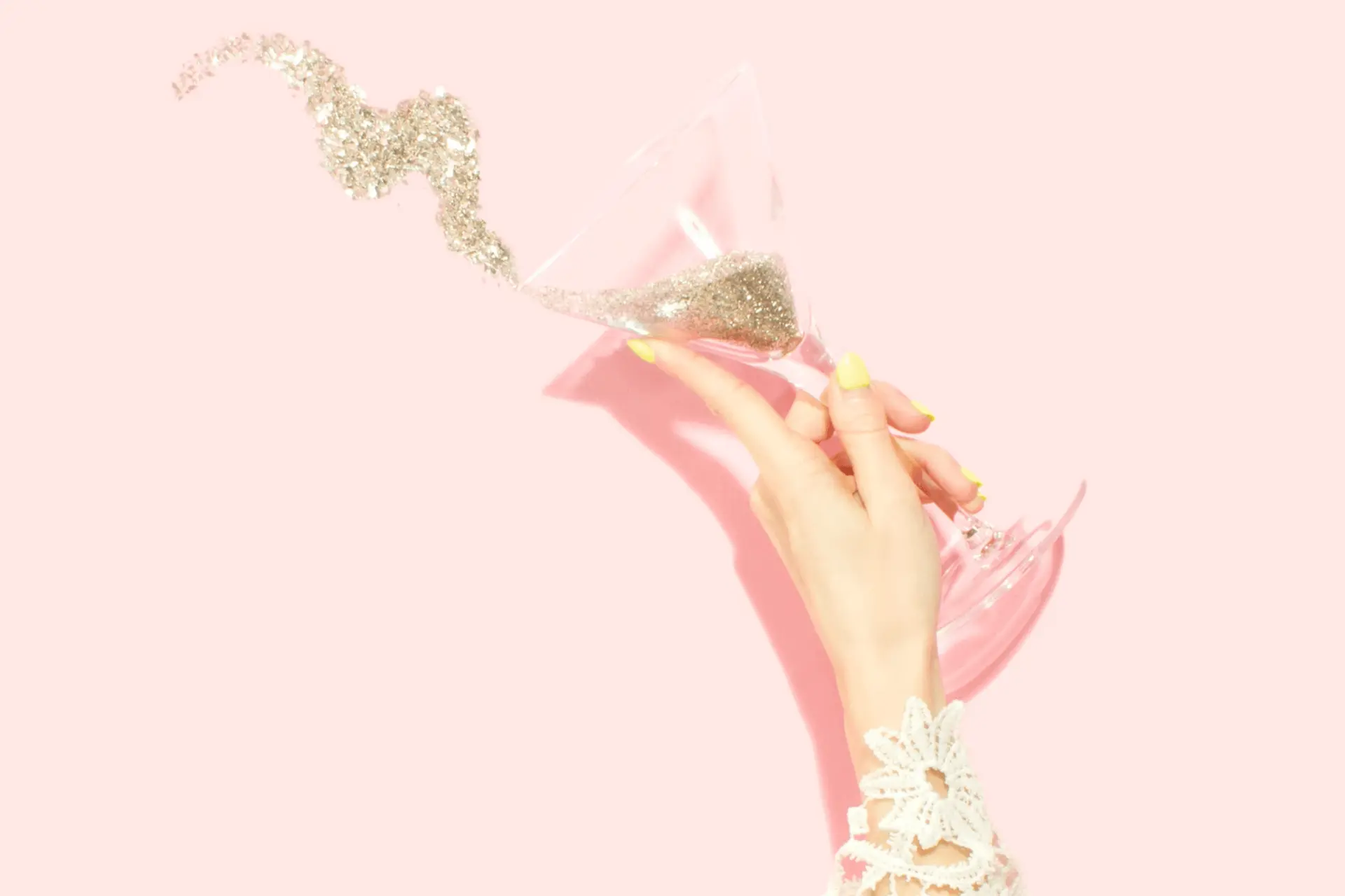 Champagne and glitter, and being held by a hand on a pink background